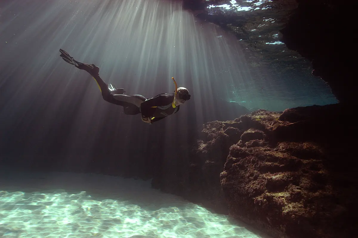 Scuba diver exploring an underwater cave in Formentera with sunlight rays filtering through the water